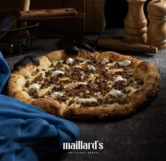 Artisanal pizza with toppings on a dark surface, featuring Maillard's Artisanal Bread logo.