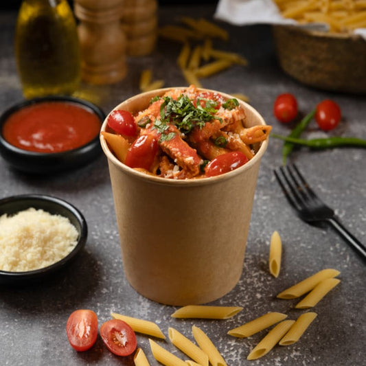 Pasta dish in a paper cup with ingredients on a dark surface