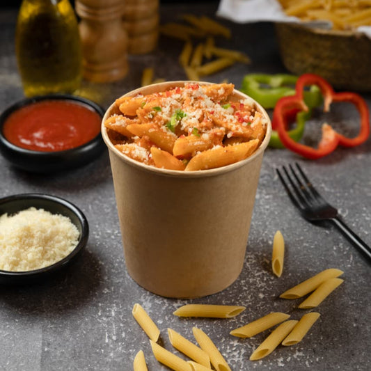 Penne pasta in a paper cup with ingredients on a dark surface