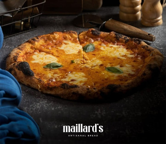 Cheesy pizza with basil leaves on a dark surface, featuring the Maillard's logo.