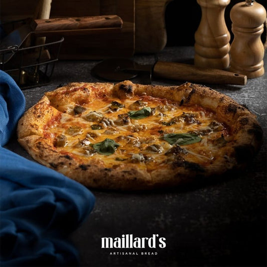 Pizza with cheese and greens on a dark surface, featuring Maillard's Artisanal Bread logo.