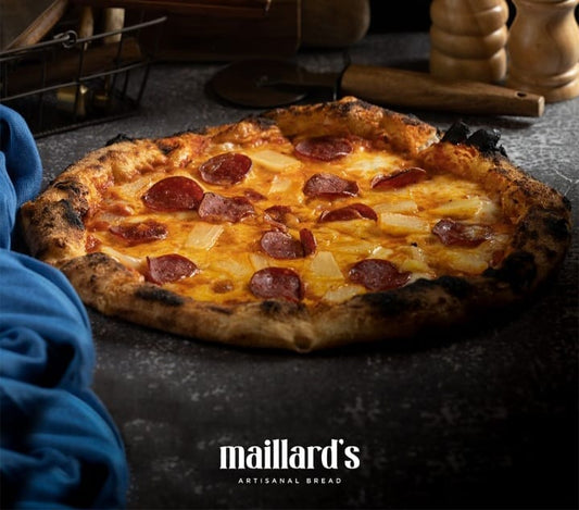 Pepperoni and pineapple pizza on a dark surface with 'maillard's' branding.