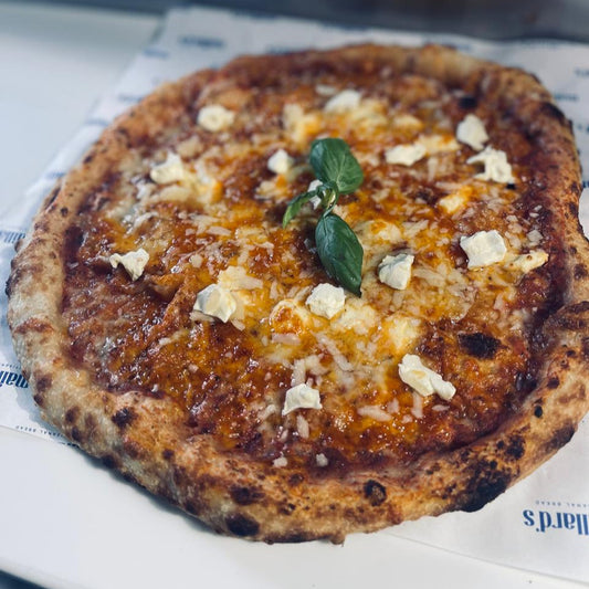 Small pizza with cheese and a leaf on top, placed on a newspaper.