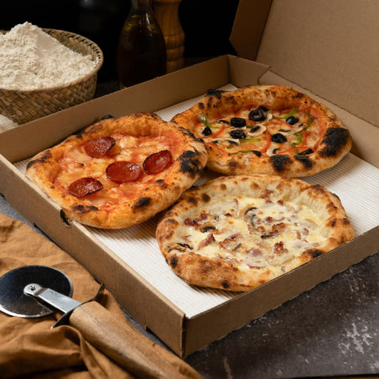 Three pizzas in a cardboard box with a dark background