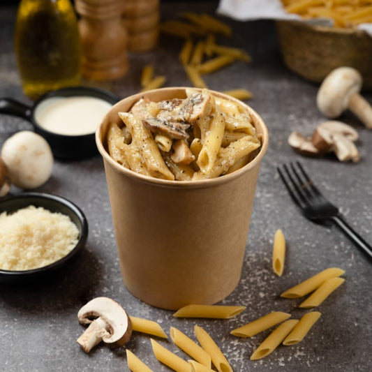 Pasta dish in a paper cup with ingredients on a dark surface